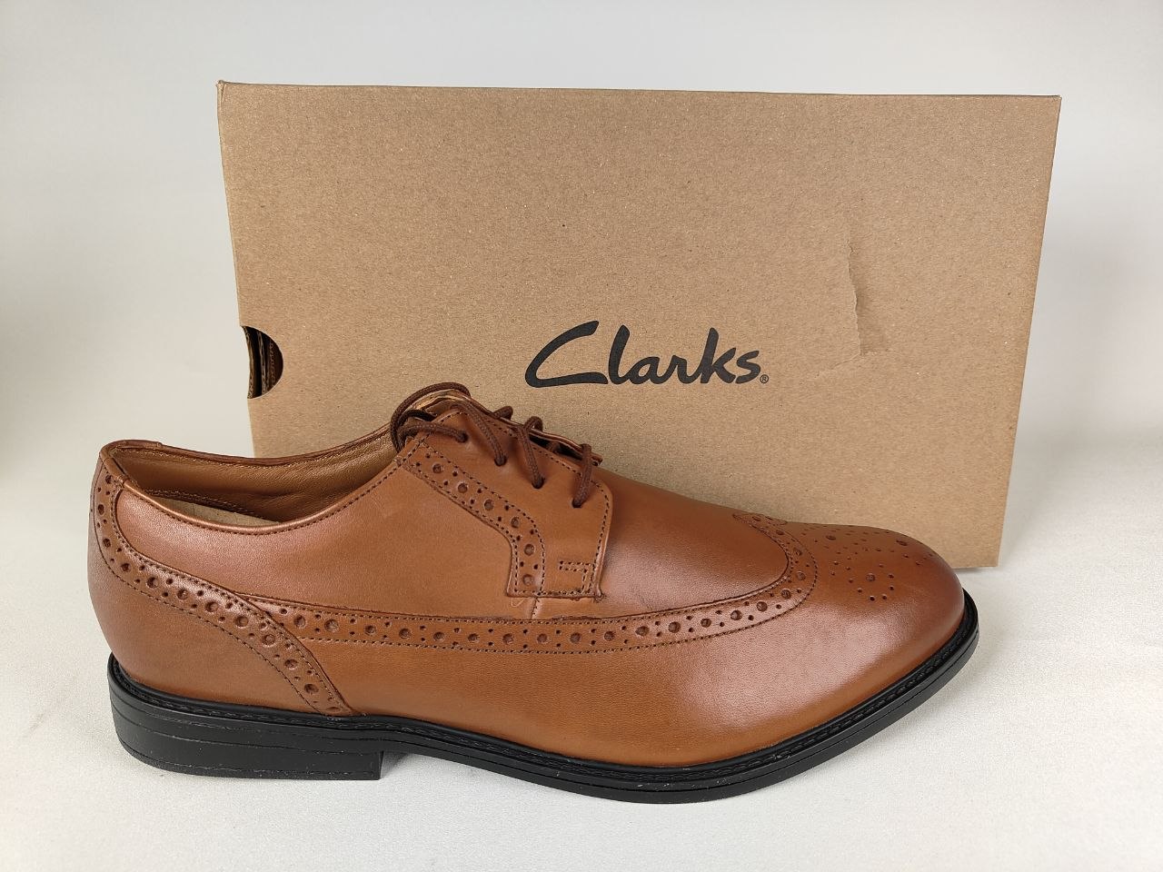 A Clarks Beckfield Limit Men's Tan Leather Wingtip Brogue shoe in front of a Clarks branded box on a white background - Brand shot @runinrain