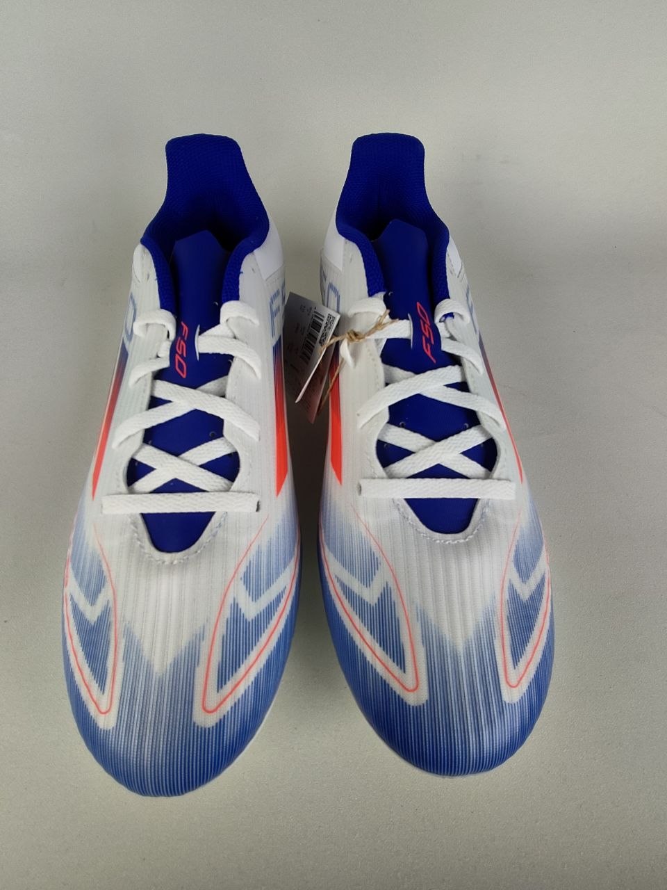 Pair of blue and white Adidas F50 Club FxG shoes on a gray background - Front view @runinrain