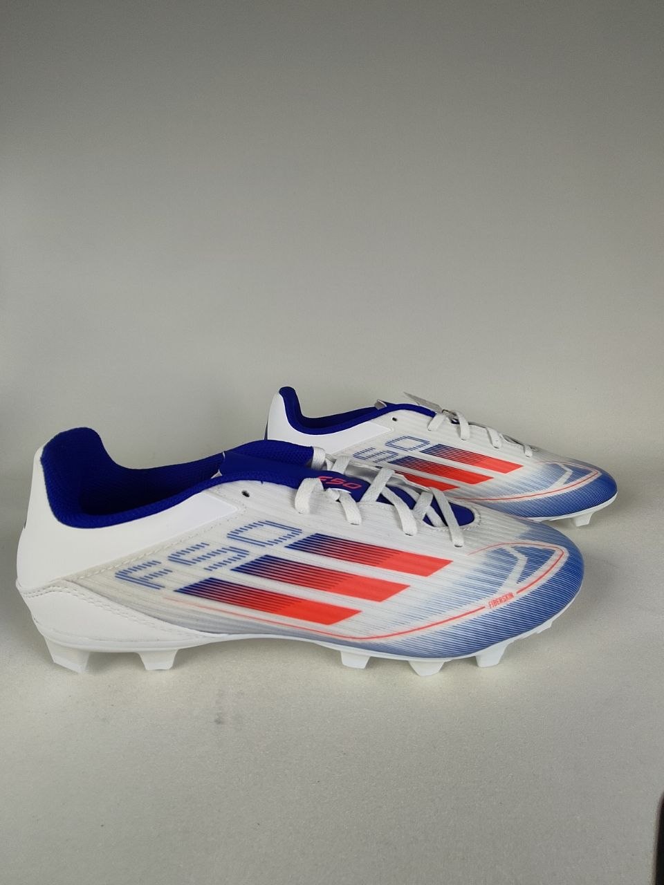 A pair of Adidas F50 Club FxG multi-ground football boots in white, red, and blue, pro-speed soccer cleats | RunInRain