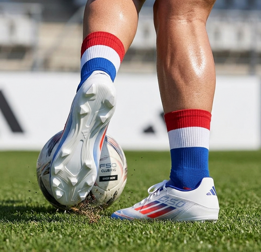 Person wearing red, white, and blue striped socks and white Adidas F50 Club FxG cleats on a grass field - free style @runinrain