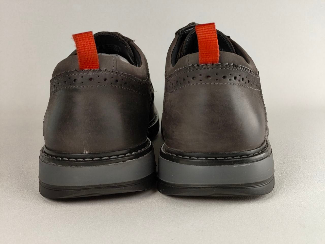 Pair of dark brown shoes with red laces on a light gray background