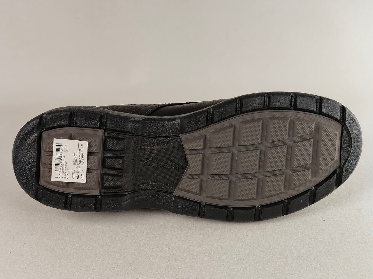 Black shoe sole with tread pattern and a visible brand label on a light gray background