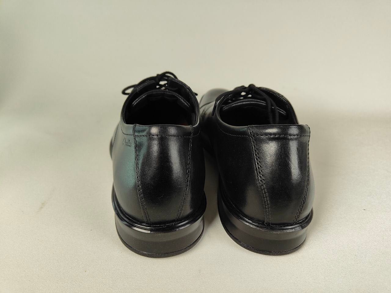 A pair of Clarks Bensley Cap Men's Black Leather Oxford shoes on a light gray background – rear view @RunInRain  