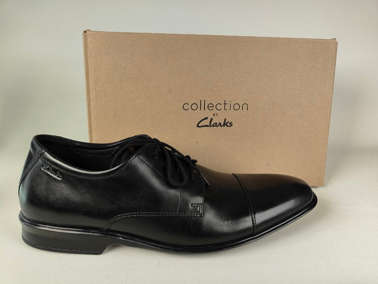 A Clarks Bensley Cap Men's Black Leather Oxford shoe in front of a Clarks Collection branded box on a light gray background - Side shot @runinrain