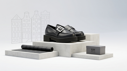 Black GCDS x Clarks 1 – Limited Edition Leather Loafers on a white platform with a box and rolled fabric, against a light gray background.