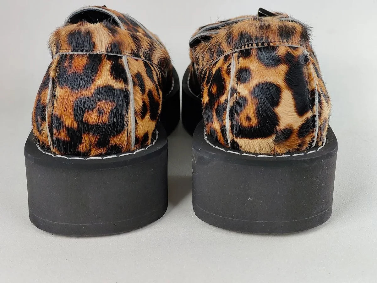 Pair of shoes with leopard print fur and black platform soles on a light gray background