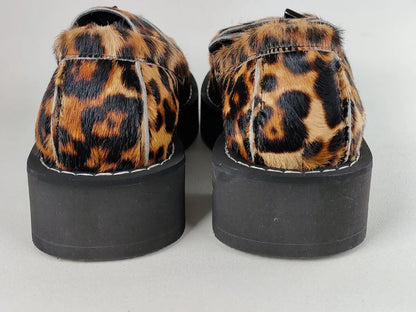 Pair of shoes with leopard print fur and black platform soles on a light gray background