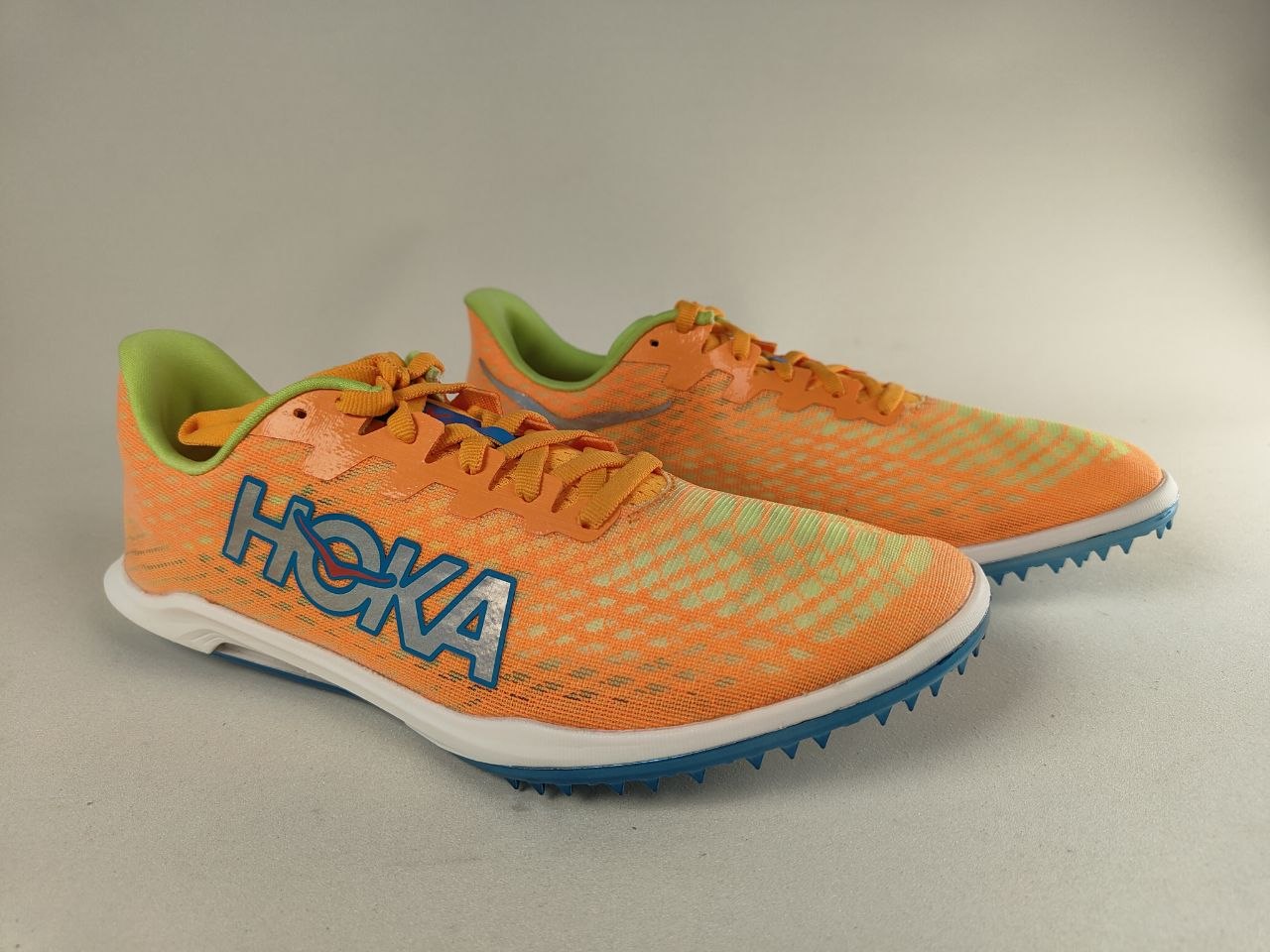A pair of orange HOKA Cielo X 2 MD running shoes with blue soles on a gray background - 3/4 view