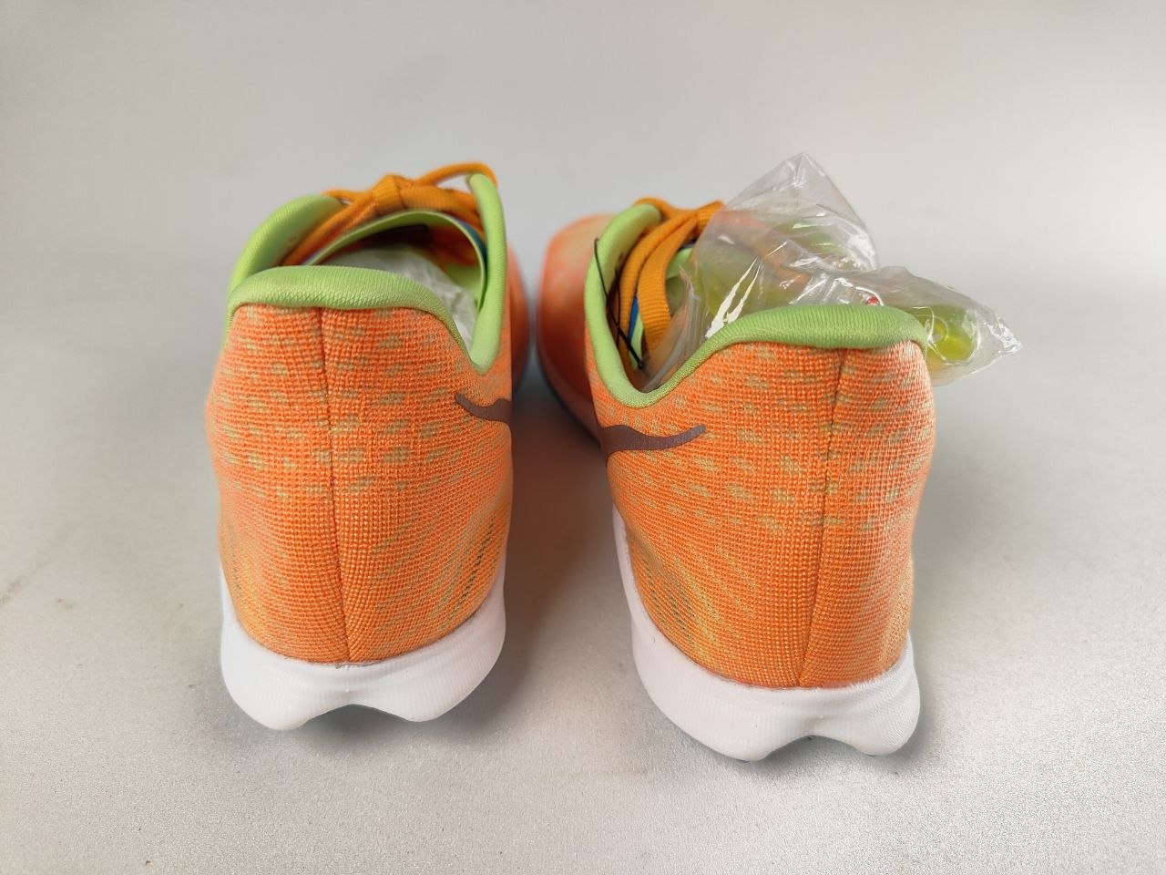 Pair of orange HOKA Cielo X 2 MD track spikes with green accents on a light gray background