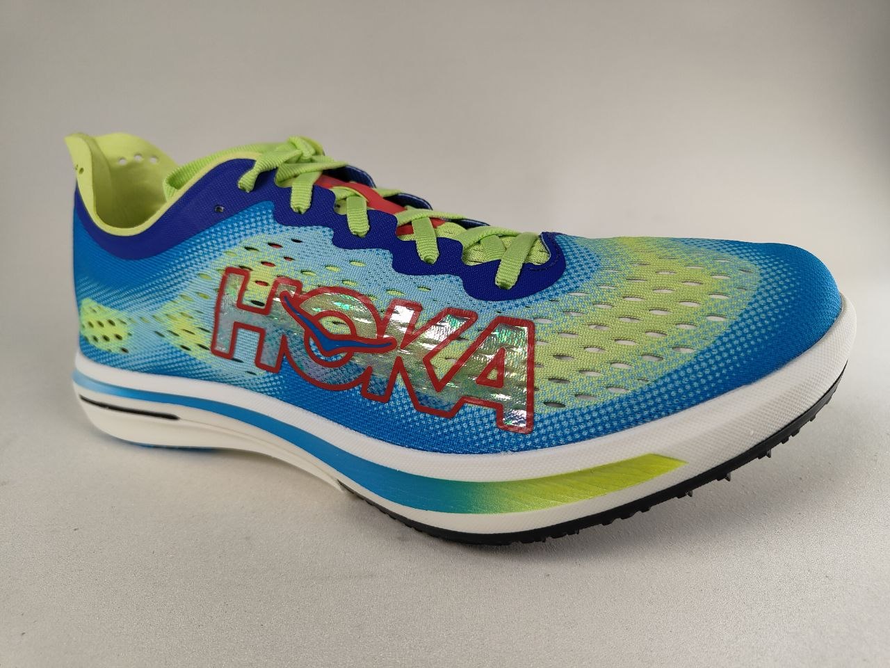 A Hoka Cielo FlyX Carbon-Plated Track Spikes Cyan/Lime shoe with 'Hoka' branding on a gray background – 3q View @RunInRain