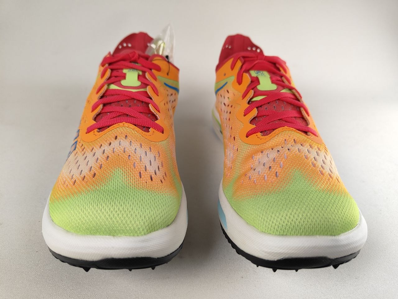 A pair of Hoka Cielo FlyX Carbon-Plated Track Spikes Solar Flare with a gradient design on a light gray background – Front View @RunInRain 