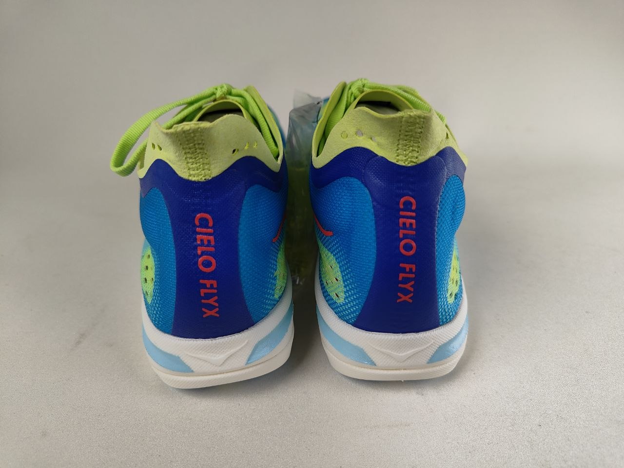 A pair of Hoka Cielo FlyX Carbon-Plated Track Spikes Cyan/Lime shoes with 'CIELO FLYX' branding on a light gray background – Rear View @RunInRain 