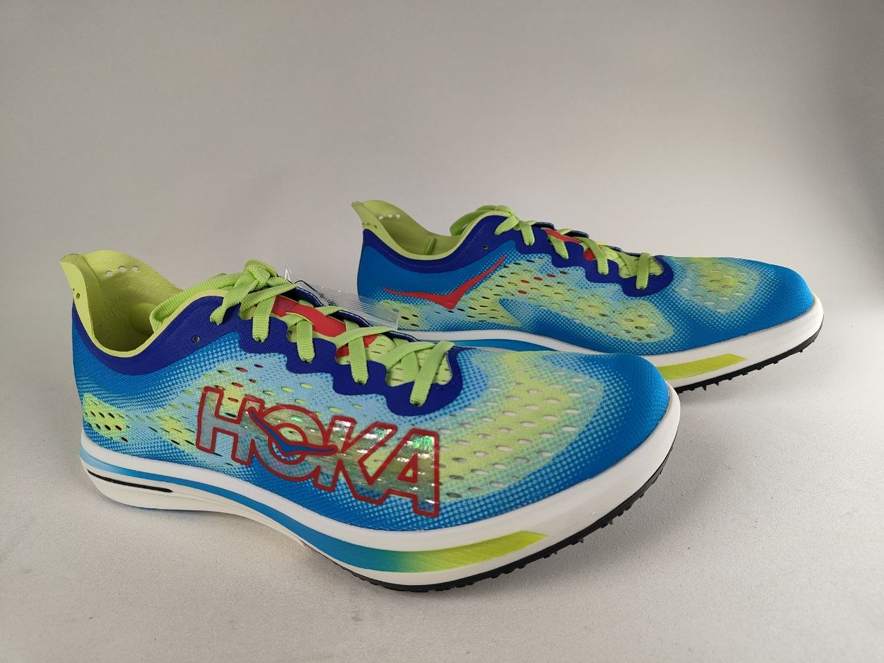 A pair of Hoka Cielo FlyX Carbon-Plated Track Spikes Cyan/Lime shoes with 'Hoka' branding on a gray background – Side View @RunInRain