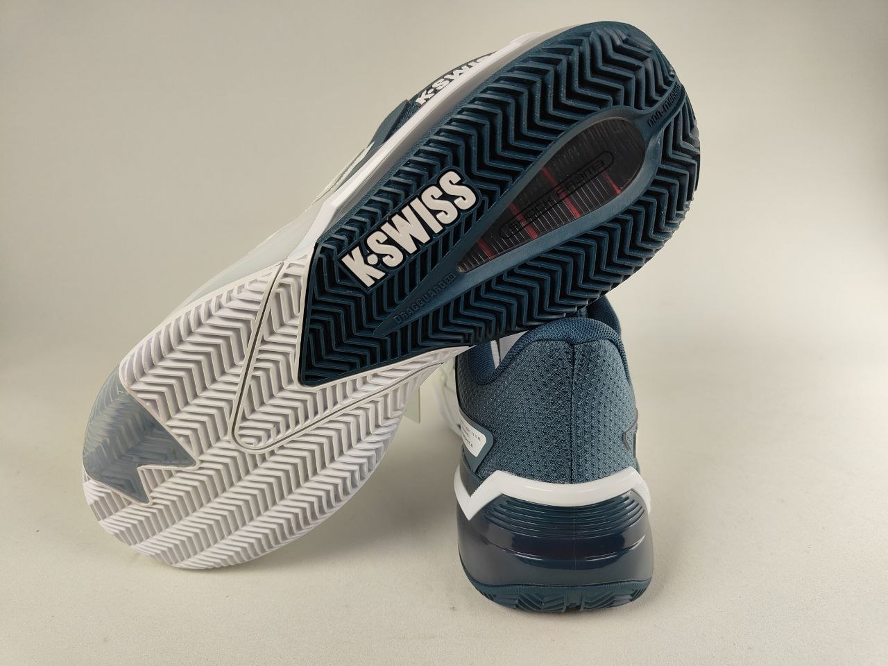 K-Swiss Ultrashot 4 men's clay court tennis shoe in white and dark blue, durable grip outsole for clay surfaces. a focus on the sole and brand logo - Rear Sole view @RunInRainwith.