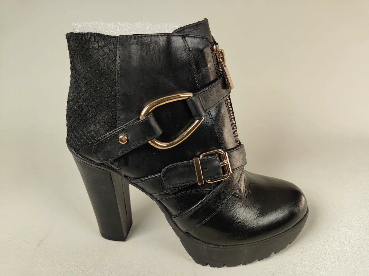 Black high-heeled La Strada Elite Ankle Boot in black leather with gold buckles on a light gray background - side view @runinrain