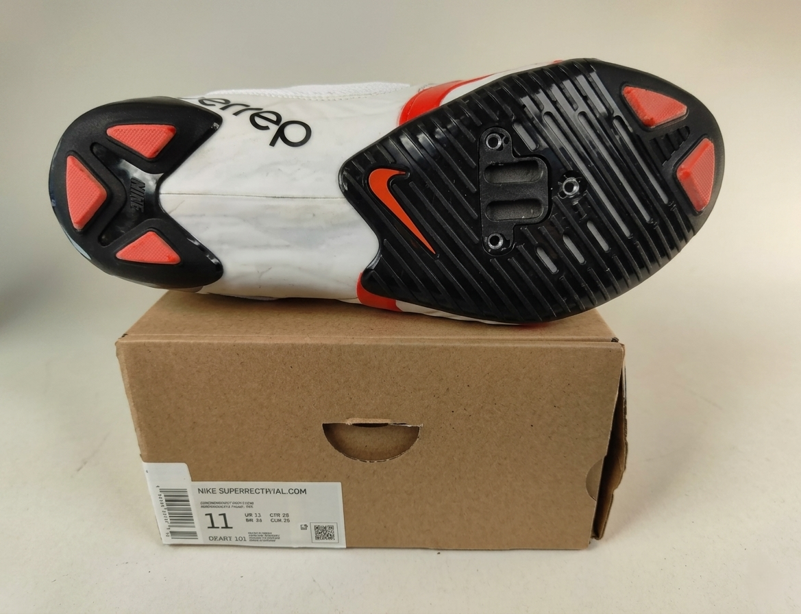 Sole of a Nike SuperRep Cycle 2 NN Indoor Cycling Shoe White/Black with red and black design on a cardboard box  on a light gray background – Sole detail View @RunInRain