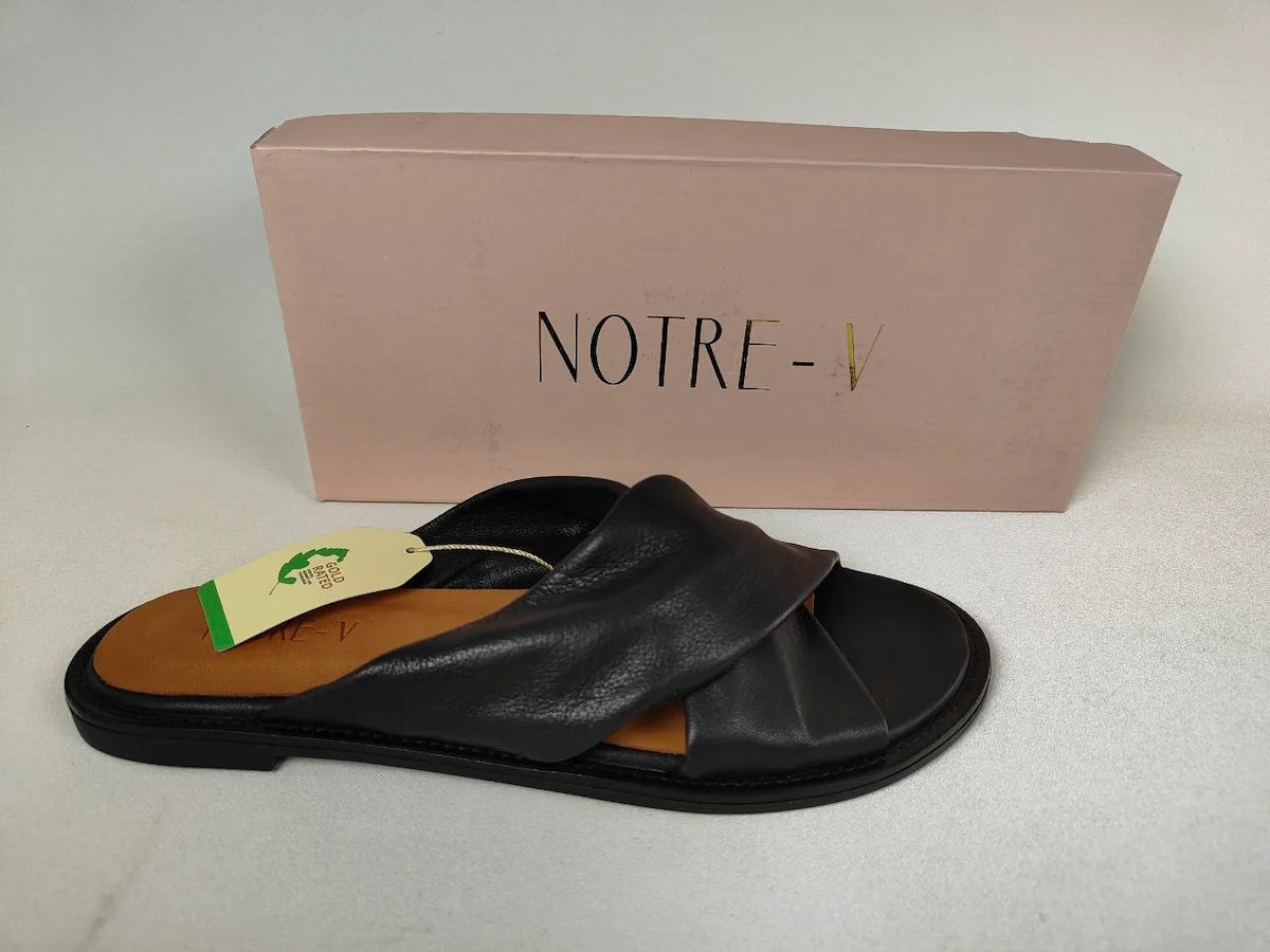 A black Notre-V Elegant Criss-Cross Black Leather Women's sandal with open toe on a light gray background with a visible brand tag and pink box labeled 'NOTRE' in the background - Brand Shot @runinrain