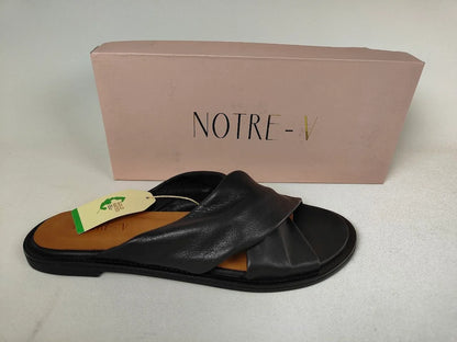 A black Notre-V Elegant Criss-Cross Black Leather Women's sandal with open toe on a light gray background with a visible brand tag and pink box labeled 'NOTRE' in the background - Brand Shot @runinrain