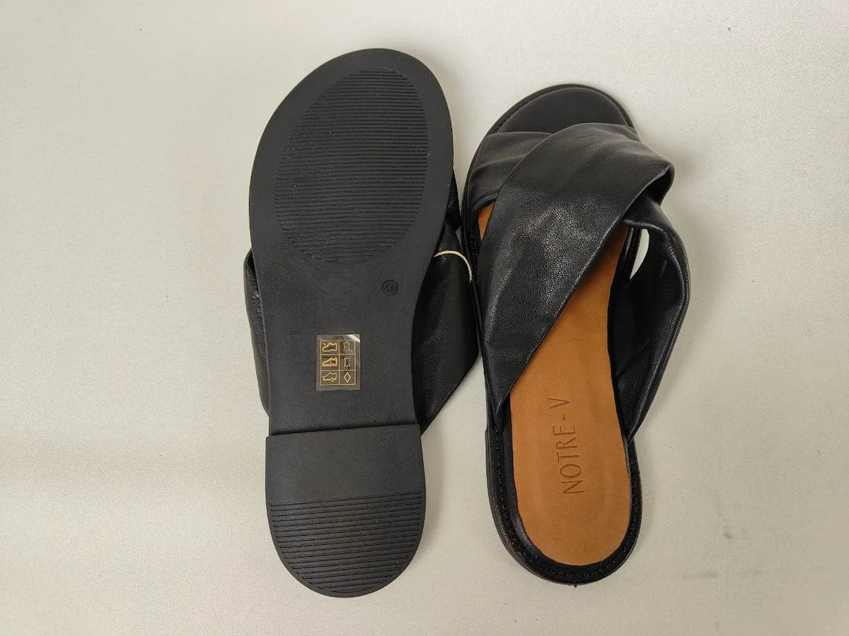 A black sole of Notre-V Elegant Criss-Cross Black Leather Women's sandal beside another Notre-V Elegant Criss-Cross Black Leather Women's sandal on a light gray background – Sole View @RunInRain